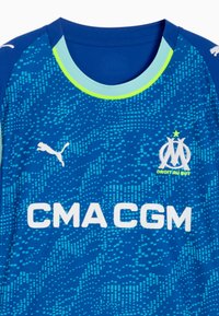 Niebieski sportowy strój z jasnoniebieskim i neonowozielonym kołnierzykiem, biały logo Puma na prawej piersi, herb klubu Marseille na lewej piersi oraz tekst sponsora CMA CGM.