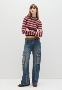 Gestreifter, gerippter Rollkragenpullover in Pink und Maroon, kombiniert mit weitgeschnittenen blauen Jeans-Cargohosen mit mehreren Taschen und einem braunen Gürtel.