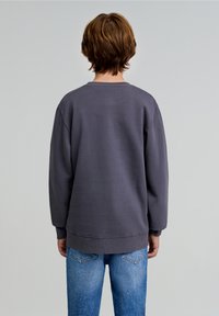 Grijze sweatshirt met een ronde hals, afhangende schouders en ribgebreide boorden, gecombineerd met lichtblauwe slimfit jeans. Eenvoudig en casual ontwerp.