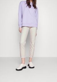 Fialová mikina, béžové zkrácené džíny, bílé nazouvací boty s černými podrážkami. Měkká tkanina, volný střih a minimalistický design.