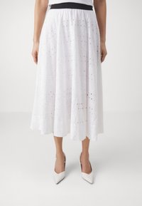 Fustă midi albă cu un model din ochiuri, având o talie neagră. Țesătura pare texturată și ușoară, desfăcându-se ușor la tiv.