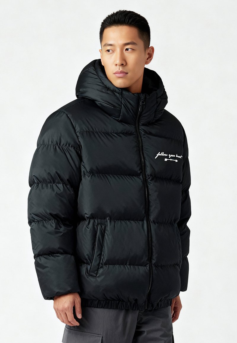 Zwarte pufferjas met een hoge kraag, ritssluiting, voorzakken en geborduurde tekstdetails. Heeft een gladde, glanzende textuur.