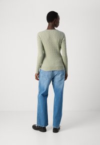Maglione a cavo a coste verde chiaro con silhouette aderente, abbinato a jeans blu a vita alta e dalla vestibilità morbida, insieme a scarpe nere.