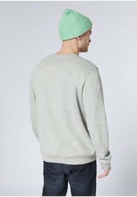 Light gray sweatshirt with long sleeves, crew neck, and ribbed cuffs, paired with dark denim jeans. Worn with a mint green beanie.