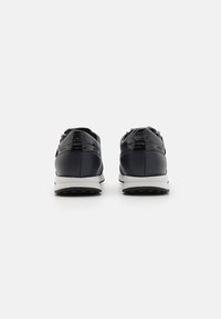 Schwarze synthetische Sneakers mit glatter Textur, weißer Sohle und einem Reißverschluss an der Ferse. Minimalistisches Design, ergonomische Form.