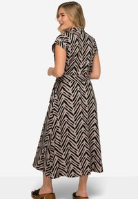 Schwarz-beige gestreiftes Kleid im Chevron-Muster mit kurzen Ärmeln, einer taillierten Taille und einem fließenden Midi-Längen-Schnitt, kombiniert mit braunen Plateausandalen.
