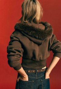 Bruine cropped hoodie met een nep bont gevoerde capuchon, geribbelde manchetten en tailleband. Draag met donkere jeans en een gestikte leren riem.