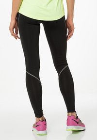 Leggings atléticos negros con costuras reflectantes, combinados con zapatillas deportivas de un vibrante color rosa y verde. Material suave y elástico para mayor comodidad.