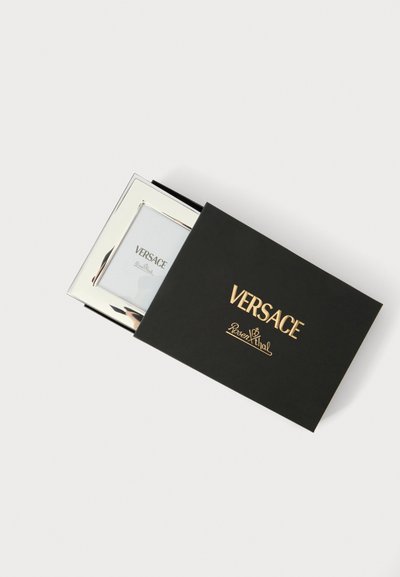 Cadre photo argenté Versace partiellement à l'intérieur d'une boîte noire avec logos dorés Versace et Rosenthal sur un fond blanc uni.