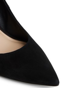 Escarpin en suédine noire à bout pointu avec une texture lisse. Présente des côtés légèrement découpés et une semelle intérieure beige.