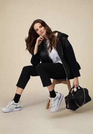 Sort quiltet jakke med hætte, hvid T-shirt, sorte bukser, hvide sneakers med sølvdetaljer og en sort håndtaske med kædestrop.