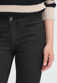 Jean en denim noir taille haute avec poches avant et fermeture à bouton en métal, associé à un pull en tricot rayé bleu marine et crème.