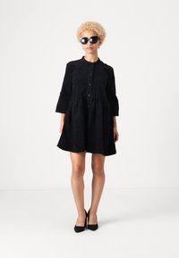 Melnas pogām apģērbtas kleitas ar teksturētu leoparda rakstu, trīs ceturtdaļu piedurknēm un izplestu svārku. Pievienotas melnas saulesbrilles un papēži.