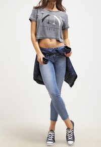 Grå croppad t-shirt med stor svart text, blå skinny jeans och marinblå sneakers. Denimjacka knuten runt midjan.