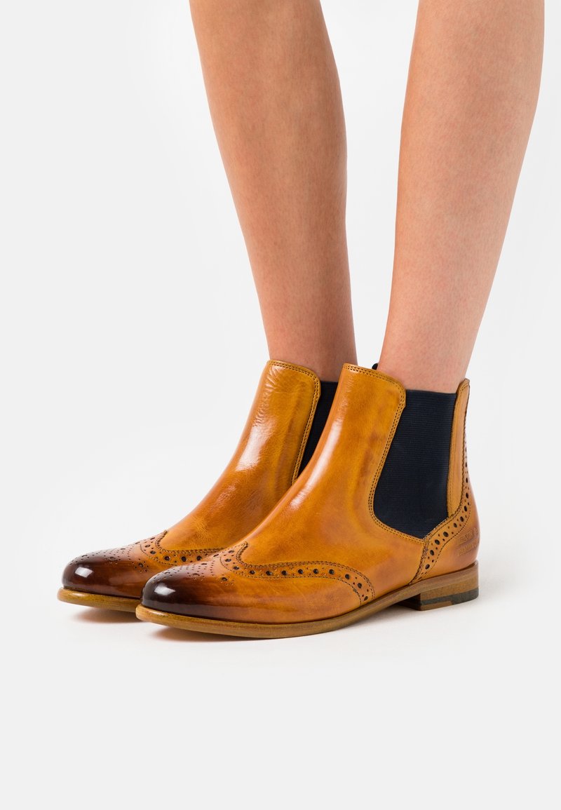 Botas Chelsea de cuero marrón claro con puntera brillante, detalles perforados en la parte delantera y paneles laterales elásticos para mayor comodidad al ponerlas.