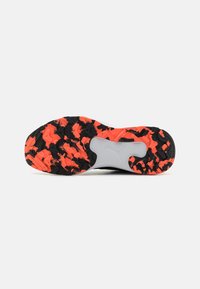 Semelle de chaussure texturée noire et orange avec un motif distinctif, fabriquée en matériau en caoutchouc et avec une accentuation blanche près du talon.