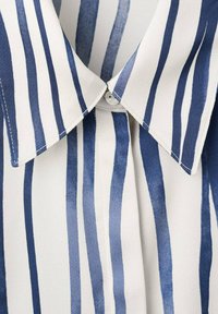 Modra in bela srajca z navpičnimi črtami in koničastim ovratnikom. Narejena iz lahkega blaga, z gumbom na vratu in mehko teksturo.