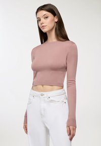 W krótkiej wersji, długiej bluzce z miękkiego różowego materiału, z okrągłym dekoltem, zestawionej z białymi dżinsami z zapięciem na guzik i szlufkami na pasek.