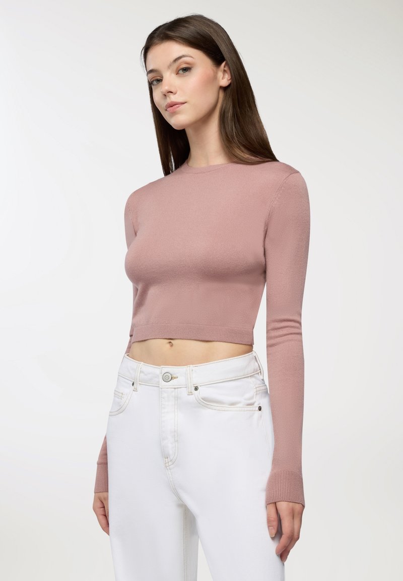 W krótkiej wersji, długiej bluzce z miękkiego różowego materiału, z okrągłym dekoltem, zestawionej z białymi dżinsami z zapięciem na guzik i szlufkami na pasek.