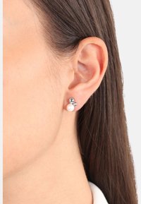 Oreja de mujer con cabello castaño oscuro, lleva pendientes de arete de plata con una perla y una pequeña gema clara.