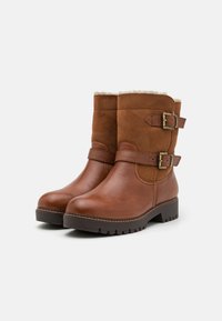 Braune Leder- und Wildlederstiefel mit verschiedenen Texturen, ausgestattet mit zwei seitlichen Schnallen und einem Pelzbesatz oben, sowie einer robusten Profilsohle.