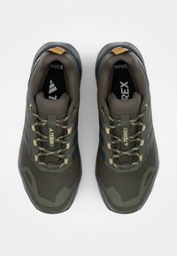 Par de zapatillas de senderismo Terrex en verde oliva y negro con detalles y cordones beige, vistas desde arriba sobre un fondo blanco.