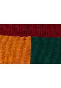Tessuto lavorato a maglia multicolore che mostra sezioni di rosso, arancione e verde. Ogni blocco di colore ha un aspetto testurizzato e a coste.
