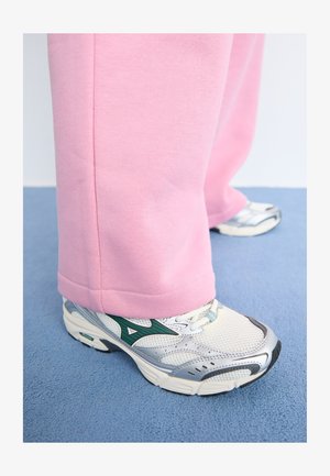 Pantalones deportivos de color rosa claro con un corte holgado, combinados con zapatos deportivos plateados y verdes que cuentan con detalles de malla y suelas texturizadas.