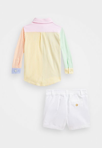 Chemise à manches longues rayée dans des couleurs pastels (rose, orange, jaune, vert) avec un poignet à bouton. Short blanc avec ceinture élastique et poche au dos.