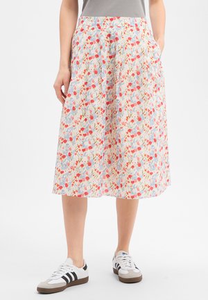 Vrouw die een witte rok tot op de knie draagt met een rood en blauw bloemenpatroon, gecombineerd met witte sneakers en een grijs topje.