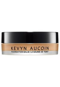 Baume Fond de Teint Kevyn Aucoin dans un contenant rond avec un couvercle noir. La base est beige avec une texture lisse et crémeuse. Le texte indique "Baume Fond de Teint."