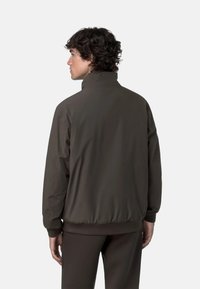 Giacca marrone leggera con colletto alto, polsini e vita elasticizzati. Texture liscia e colore uniforme, senza motivi visibili o accessori metallici.