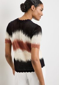 Knit short-sleeve top featuring a scalloped neckline and a gradient pattern in black, cream, and rust colors with a textured finish.