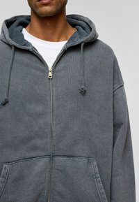 Grijze rits-hoodie met een grote voorzak, trekkoorden en een zachte textuur. Voorzien van een gouden rits en contrasterende voering van de capuchon.