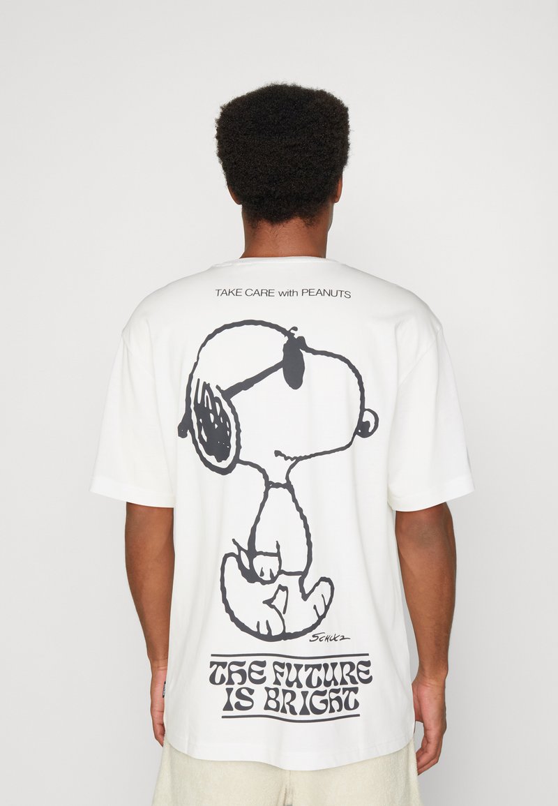 T-shirt en coton blanc avec un grand graphique noir de Snoopy au dos, accompagné du texte "L'AVENIR EST PROMETTEUR" en dessous. Manches courtes.