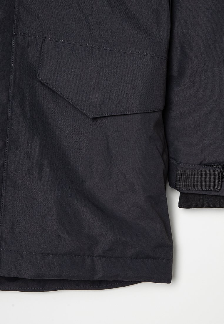 Dunkelblaue Jacke aus strukturiertem Stoff mit einer Klappentasche und einem Klettverschluss am Bündchen. Klare Linien ohne sichtbare Muster.