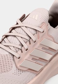 Detailní záběr růžové pletené běžecké boty s překříženými tkaničkami a třemi bílými pruhy na boku.