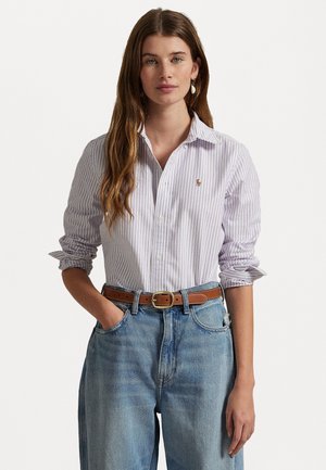 Camicia a maniche lunghe a righe in lilla chiaro e bianco, abbinata a jeans blu sbiaditi a vita alta e una cintura in pelle marrone.