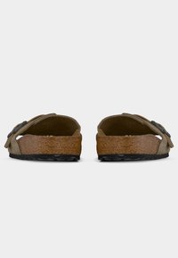 Ζευγάρι μπεζ σαμουά πεδιλάκια με πάτους από φελλό και μαύρες ρυθμιζόμενες αγκράφες, απεικονιζόμενα από πίσω σε λευκό φόντο.