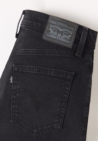 Jean Levi's noir montrant la poche arrière avec couture signature, passant de ceinture et patch en cuir à logo au-dessus de la taille.