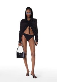 Fekete, hosszú ujjú kapucnis felső redőzött részlettel, fekete bikini alsó, kis fekete kézitáska és fekete, nyitott orrú magassarkú cipő.