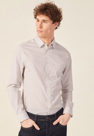 Camicia chiara a maniche lunghe con piccoli motivi geometrici e una tasca sul petto. Abbinata a jeans scuri.