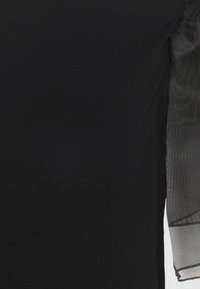Vêtement noir avec manches longues transparentes présentant de subtiles rayures verticales et un détail de poignet.