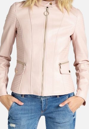 Kvinde iført en lyserød læderjakke med lynlås, quiltede detaljer og lynlåslommer, kombineret med blå slidte jeans.