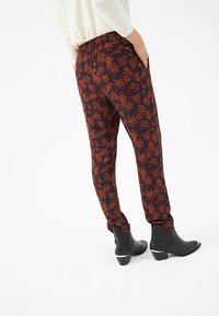 Schwarze Hosen mit einem roten Blumenmuster, elastischem Bund, zulaufendem Bein und Seitentaschen, kombiniert mit schwarzen Stiefeletten mit silbernen Akzenten.