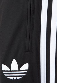 Czarne szorty sportowe z białymi paskami po bokach i haftowanym logo. Materiał jest teksturowany o gładkim wykończeniu. Zawiera kieszeń na zamek.