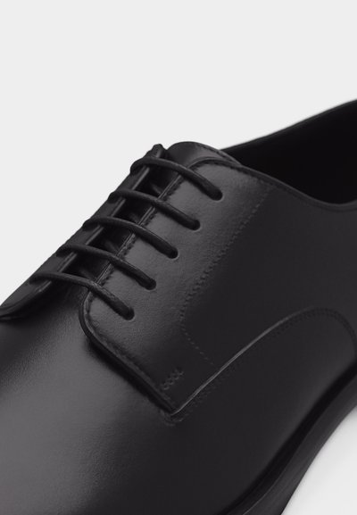 Μαύρο δερμάτινο παπούτσι οξφόρντ με κλειστό κορδόνι και λείο φινίρισμα, εμφανιζόμενο από κοντινή γωνιακή προβολή σε λευκό φόντο.
