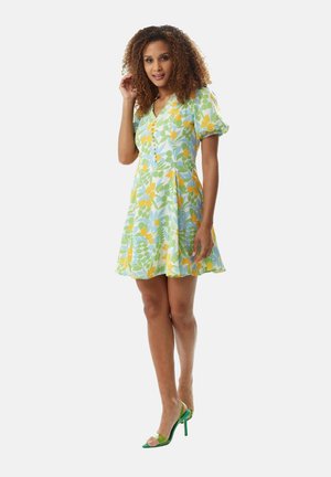 Floral dress in light blue, featuring yellow and green leaf patterns, short puff sleeves, and a v-neckline. Model paired with green high heels.