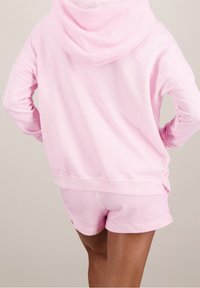 Felpa rosa con una consistenza morbida, dotata di un ampio cappuccio e polsini a coste, abbinata a pantaloni corti coordinati. Entrambi hanno cuciture rinforzate.