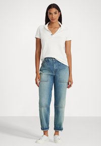 Λευκό πουκάμισο πόλο με γιακά και λεπτομέρεια κουμπιών, σε συνδυασμό με ανοιχτού μπλε τζιν ψηλής μέσης που διαθέτει μεγάλες τσέπες και γυρισμένα μπατζάκια.